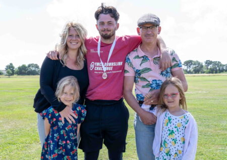 Josh, resident, smiling with his medal around his neck after finishing the challenge. He is stood with his arms around his family