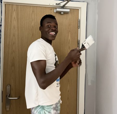 Nader, smiling holding a paintbrush while painting a room in his accommodation. He is nominated for young leader at the Youth Matters Awards