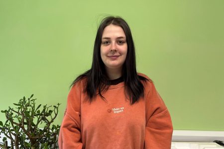 Georgia smiling against a green wall, wearing an orange jumper. She is nominated for young campaigner at the youth matters awards 2024. 